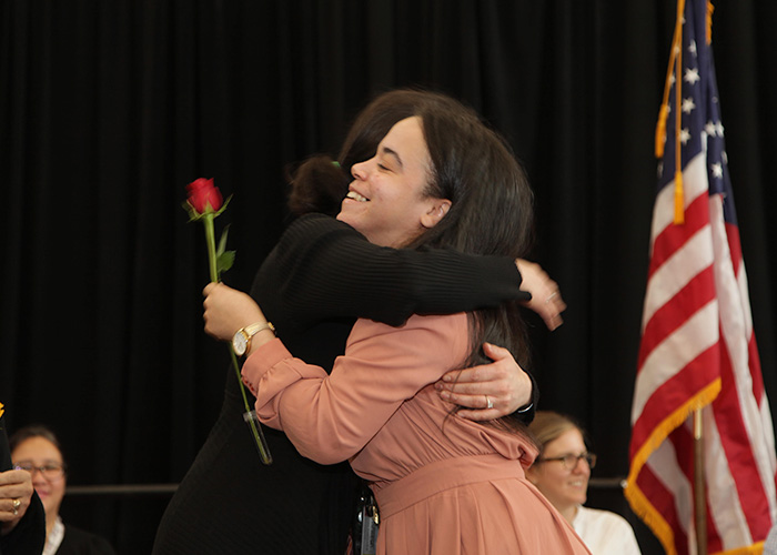 student hugging a faculty member on stage