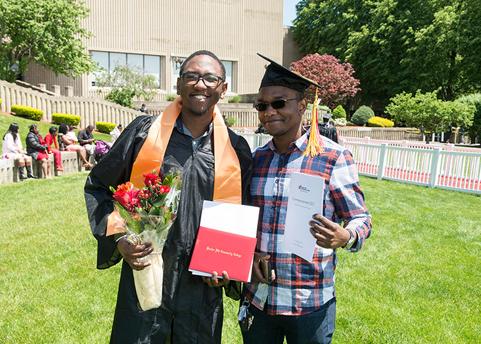 graduate poses with friend and flowers